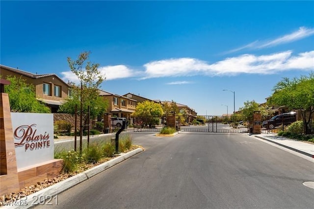 view of street featuring street lights, a gated entry, sidewalks, curbs, and a gate