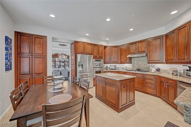 kitchen featuring stainless steel appliances, brown cabinetry, light stone countertops, and under cabinet range hood