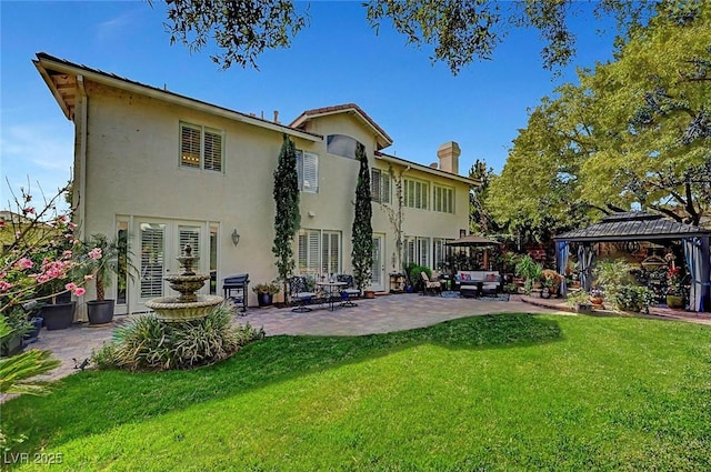 rear view of house with stucco siding, a patio, a gazebo, and a lawn