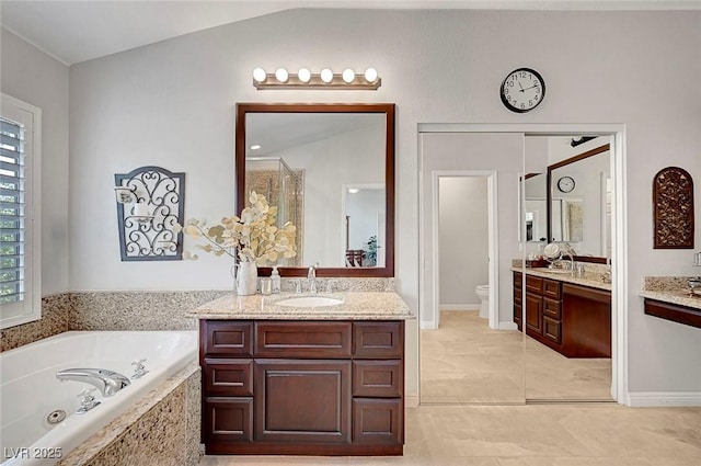 full bathroom featuring toilet, a tub with jets, two vanities, and a sink