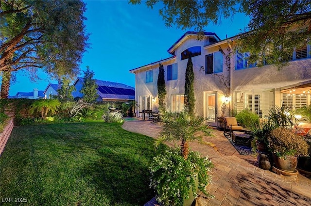 back of house featuring a patio area, a lawn, and stucco siding