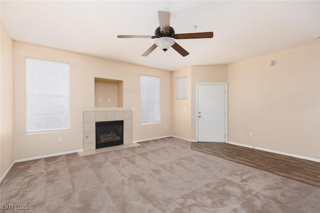 unfurnished living room featuring ceiling fan, carpet floors, a tiled fireplace, and baseboards