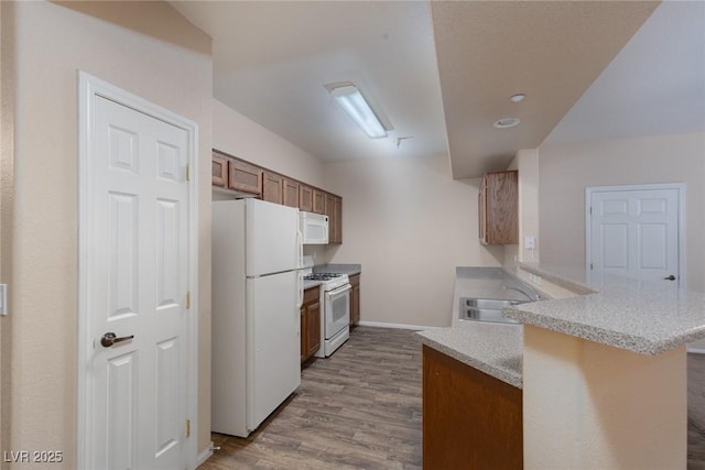 kitchen with a peninsula, white appliances, dark wood-style flooring, a sink, and light countertops