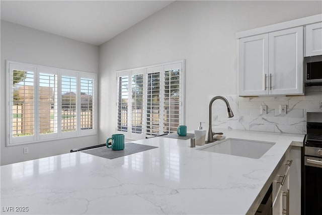 kitchen featuring light stone counters, stainless steel appliances, a sink, white cabinets, and decorative backsplash