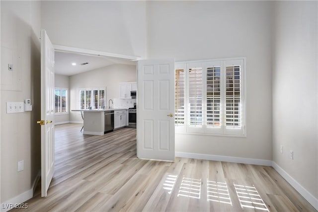 interior space with vaulted ceiling, light wood finished floors, a sink, and baseboards