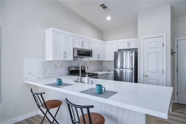 kitchen with visible vents, a kitchen breakfast bar, a peninsula, stainless steel appliances, and light countertops