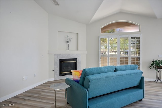 living room with lofted ceiling, wood finished floors, visible vents, baseboards, and a tiled fireplace