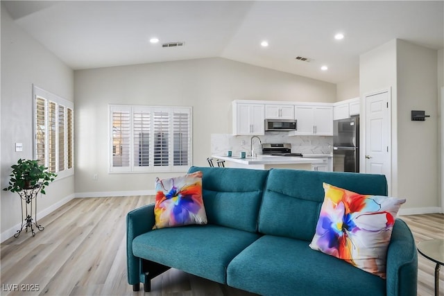 living room featuring light wood-type flooring, lofted ceiling, visible vents, and baseboards