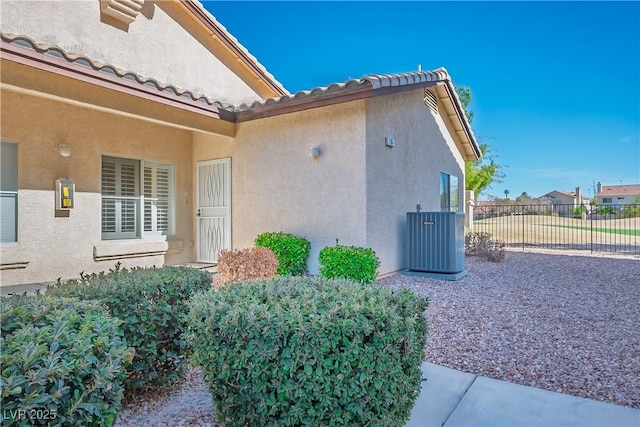 view of home's exterior featuring a tiled roof, fence, central AC, and stucco siding