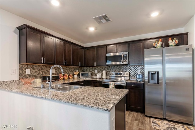 kitchen featuring stainless steel appliances, a peninsula, a sink, visible vents, and dark brown cabinets