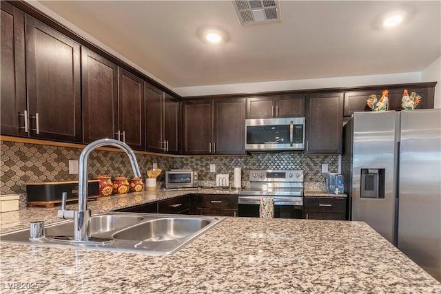 kitchen featuring visible vents, decorative backsplash, appliances with stainless steel finishes, dark brown cabinets, and a sink