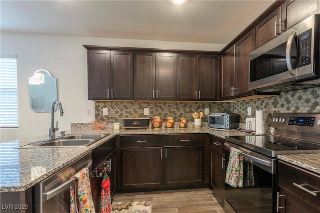 kitchen with appliances with stainless steel finishes, a peninsula, a sink, dark brown cabinets, and backsplash