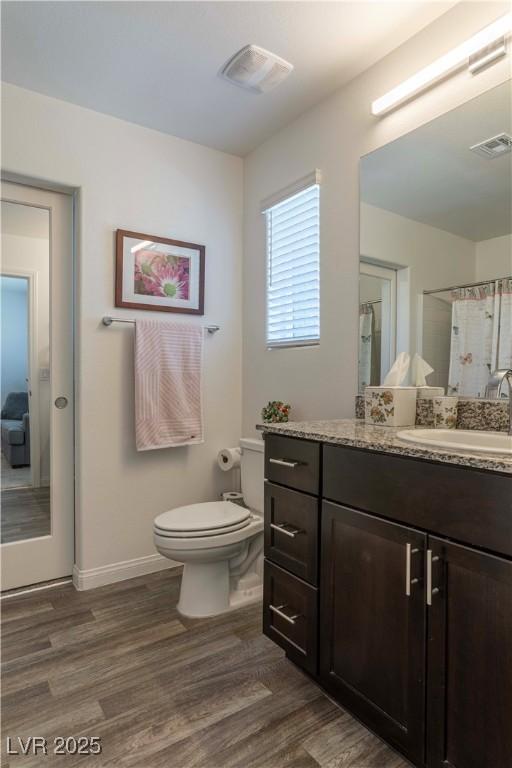 bathroom with toilet, curtained shower, wood finished floors, and visible vents