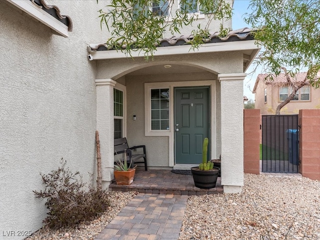 property entrance with a tile roof, a gate, and stucco siding