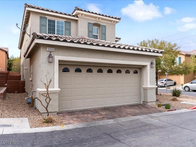 mediterranean / spanish-style home with driveway, a tiled roof, an attached garage, and stucco siding