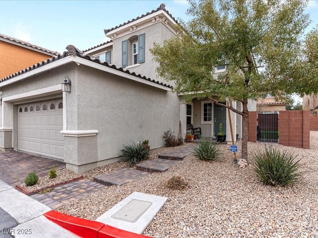 mediterranean / spanish-style house featuring decorative driveway, a tile roof, stucco siding, an attached garage, and a gate