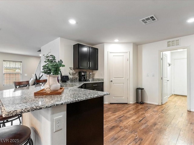 kitchen with visible vents, light wood-style flooring, light stone counters, a breakfast bar, and a peninsula