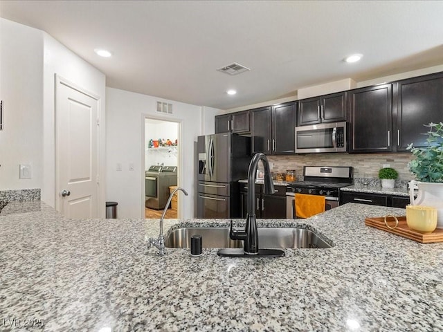 kitchen with tasteful backsplash, visible vents, appliances with stainless steel finishes, light stone countertops, and independent washer and dryer