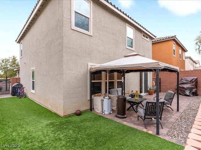 rear view of house featuring a gazebo, a patio area, fence, and stucco siding