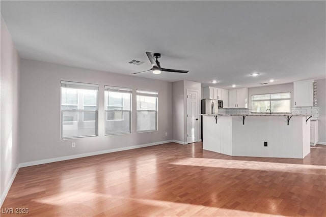 unfurnished living room with ceiling fan, a wealth of natural light, light wood-type flooring, and visible vents