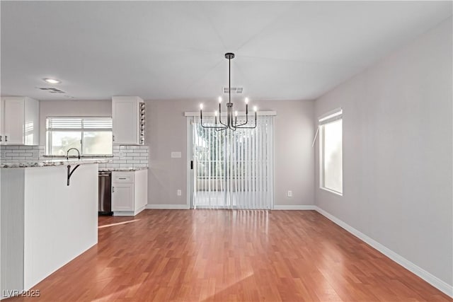 unfurnished dining area with light wood-style flooring, visible vents, a chandelier, and baseboards