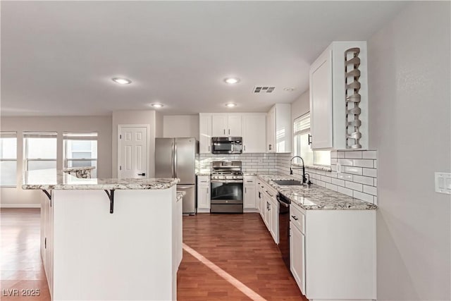 kitchen featuring visible vents, appliances with stainless steel finishes, wood finished floors, a kitchen bar, and a sink