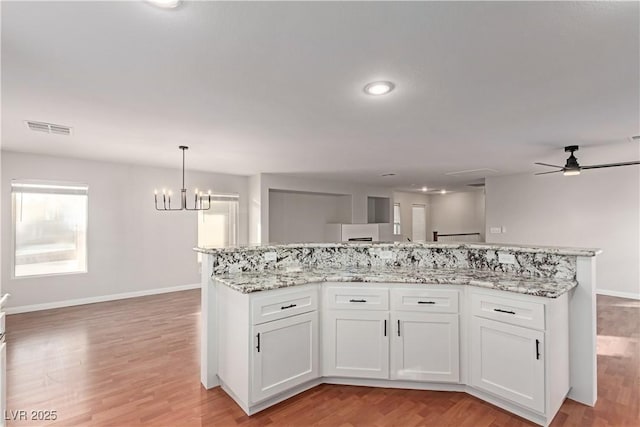 kitchen featuring visible vents, light wood-style flooring, open floor plan, white cabinets, and ceiling fan with notable chandelier