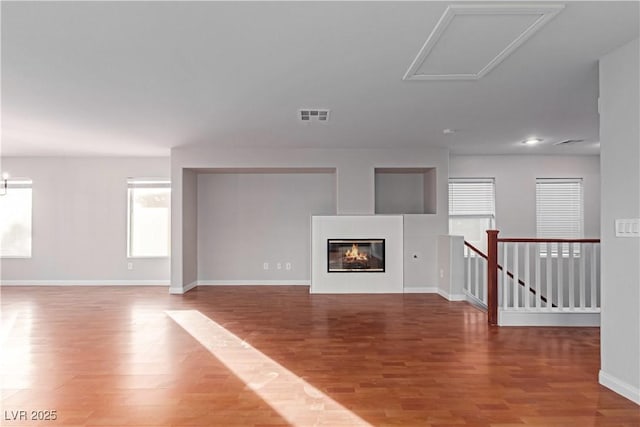 unfurnished living room with a glass covered fireplace, visible vents, baseboards, and wood finished floors