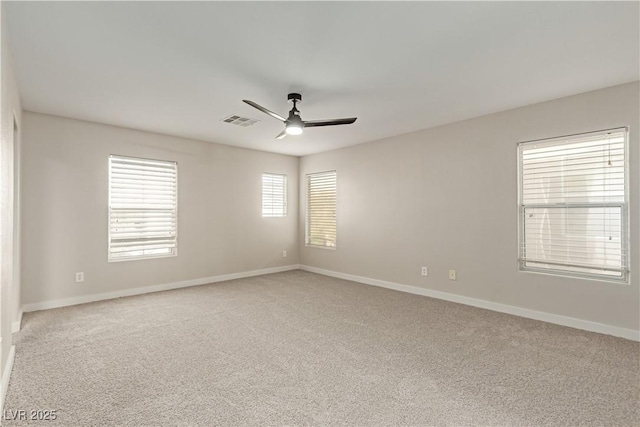 empty room featuring a ceiling fan, light colored carpet, visible vents, and baseboards