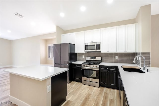 kitchen featuring stainless steel appliances, a sink, visible vents, dark cabinetry, and tasteful backsplash