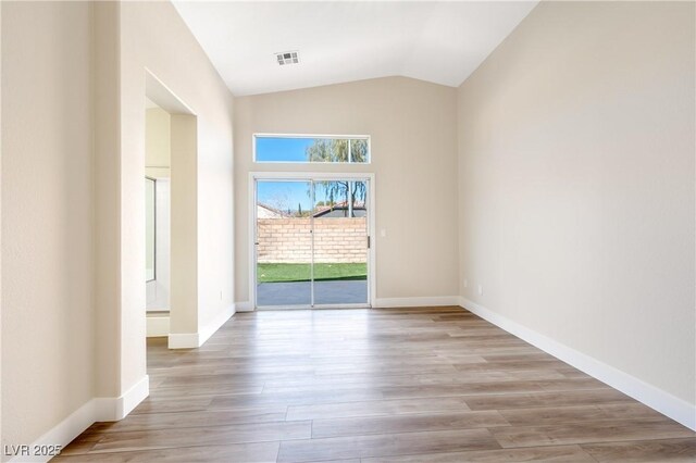 empty room with lofted ceiling, light wood-style floors, baseboards, and visible vents