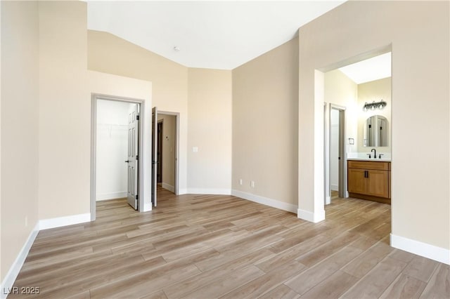 unfurnished bedroom with lofted ceiling, light wood finished floors, a sink, and baseboards