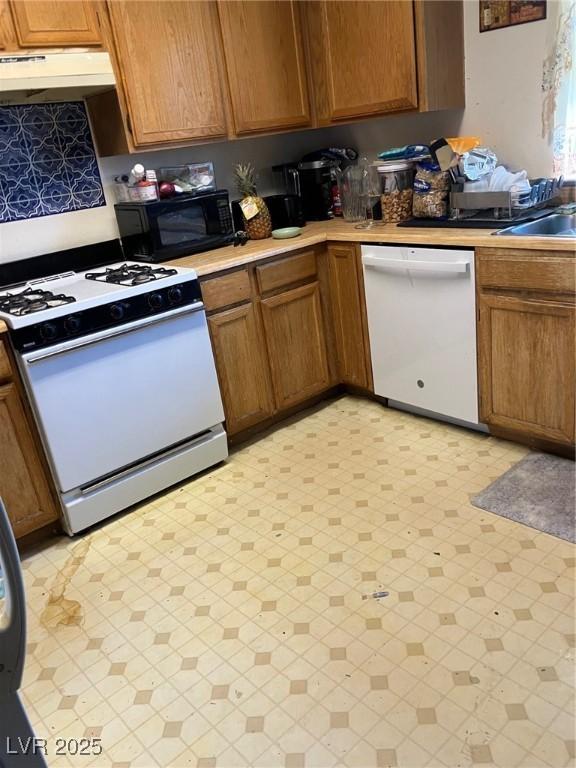 kitchen featuring under cabinet range hood, light countertops, brown cabinetry, white appliances, and a sink