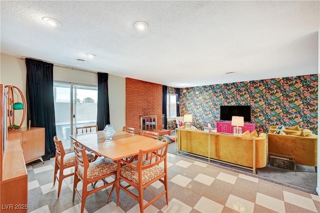 dining room with a textured ceiling, light floors, a fireplace, and wallpapered walls