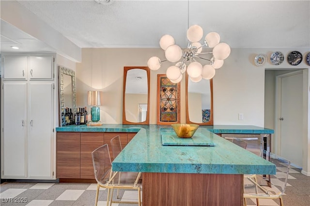 kitchen with a breakfast bar, brown cabinets, a notable chandelier, light floors, and white cabinets