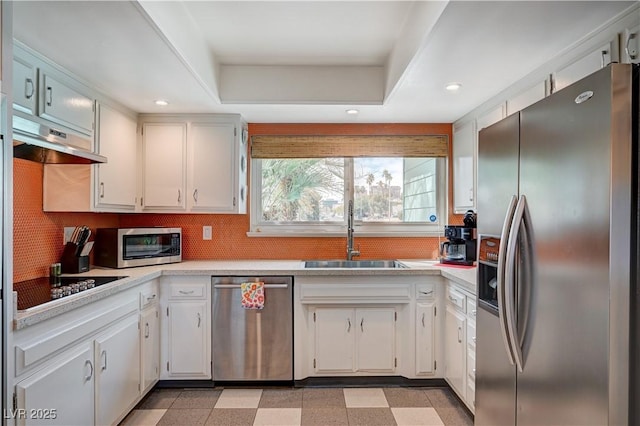 kitchen featuring stainless steel appliances, a sink, light countertops, light floors, and a tray ceiling