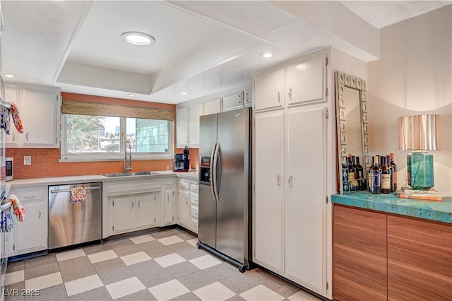 kitchen featuring stainless steel appliances, a sink, white cabinetry, light floors, and a tray ceiling