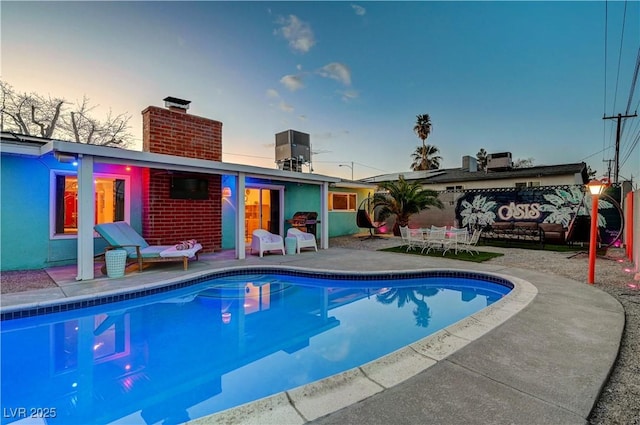 back of house at dusk with an outdoor pool, a patio, a chimney, and central air condition unit