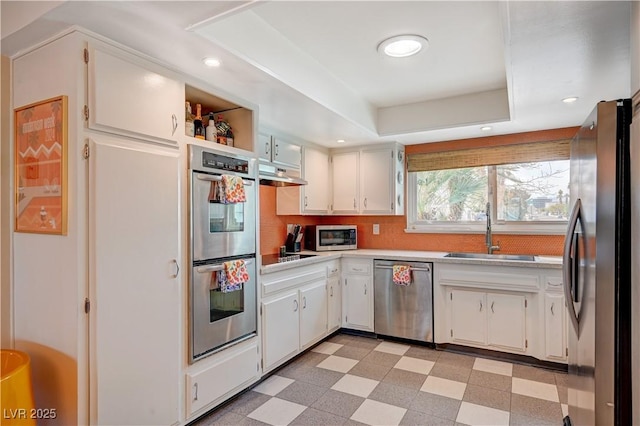 kitchen with light floors, under cabinet range hood, stainless steel appliances, and a sink