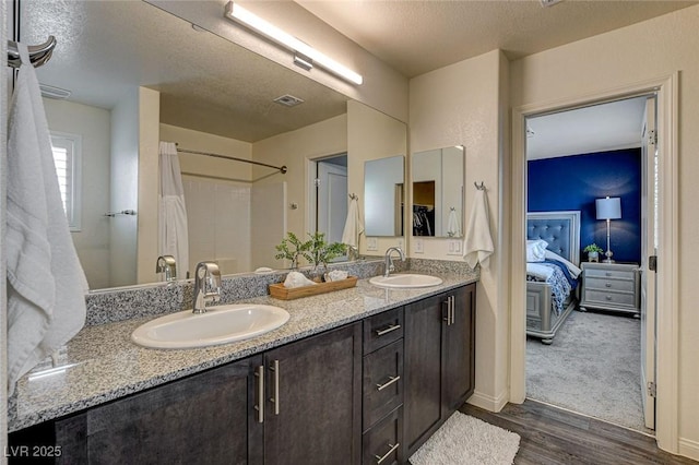 ensuite bathroom featuring double vanity, wood finished floors, a sink, and visible vents