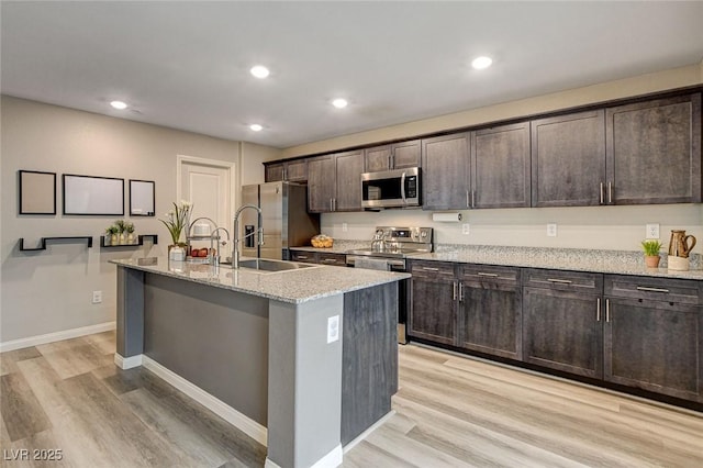 kitchen with dark brown cabinets, appliances with stainless steel finishes, a center island with sink, and light wood-style floors