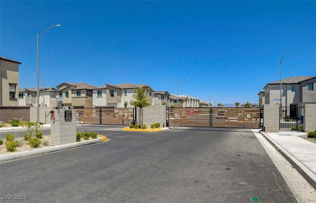 view of road featuring a residential view, a gate, a gated entry, and street lights