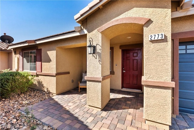 view of exterior entry with a garage and stucco siding