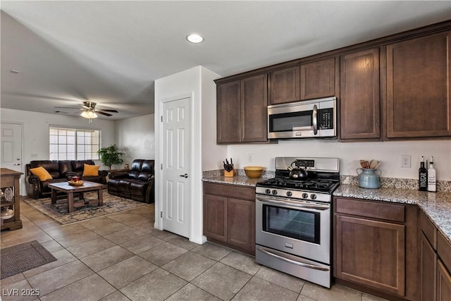 kitchen with light tile patterned floors, appliances with stainless steel finishes, open floor plan, dark brown cabinets, and light stone countertops