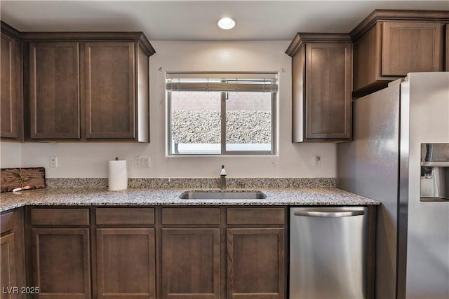 kitchen with dark brown cabinetry, light stone countertops, stainless steel appliances, a sink, and recessed lighting