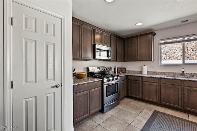 kitchen featuring light tile patterned floors, light stone counters, dark brown cabinetry, stainless steel appliances, and a sink