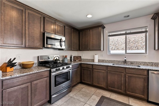 kitchen featuring light stone counters, light tile patterned floors, appliances with stainless steel finishes, a sink, and dark brown cabinets