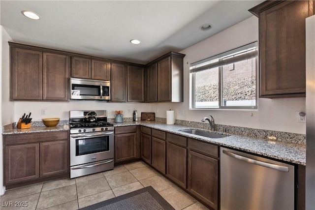 kitchen featuring light stone countertops, appliances with stainless steel finishes, dark brown cabinets, and a sink