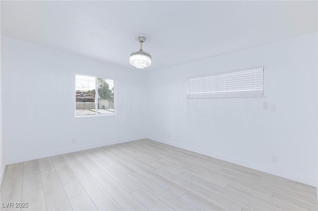 spare room with an inviting chandelier, light wood-style floors, and baseboards