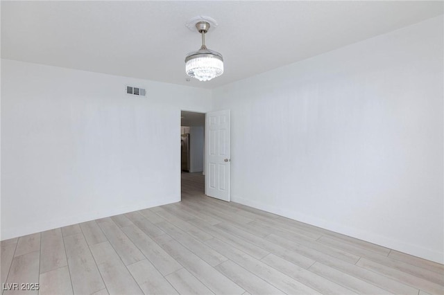 empty room with baseboards, visible vents, a notable chandelier, and light wood finished floors